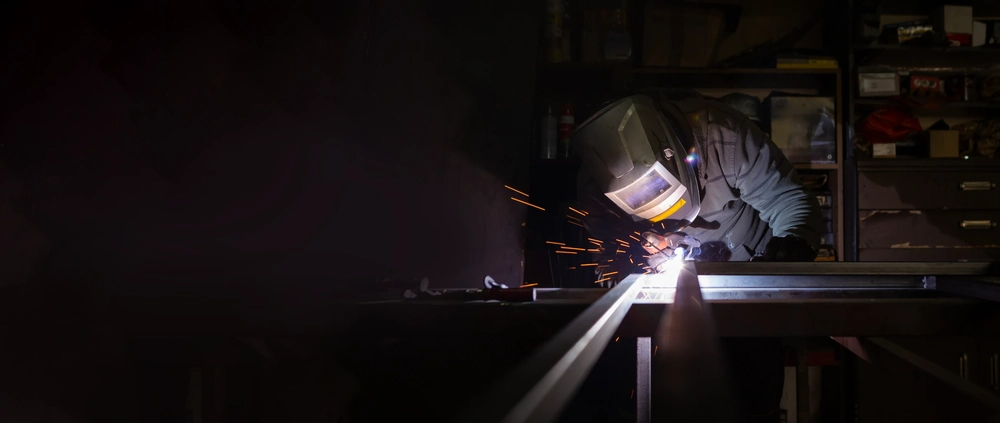 Spawacz w masce ochronnej wykonuje usługi spawalnicze przy metalowej ramie w warsztacie